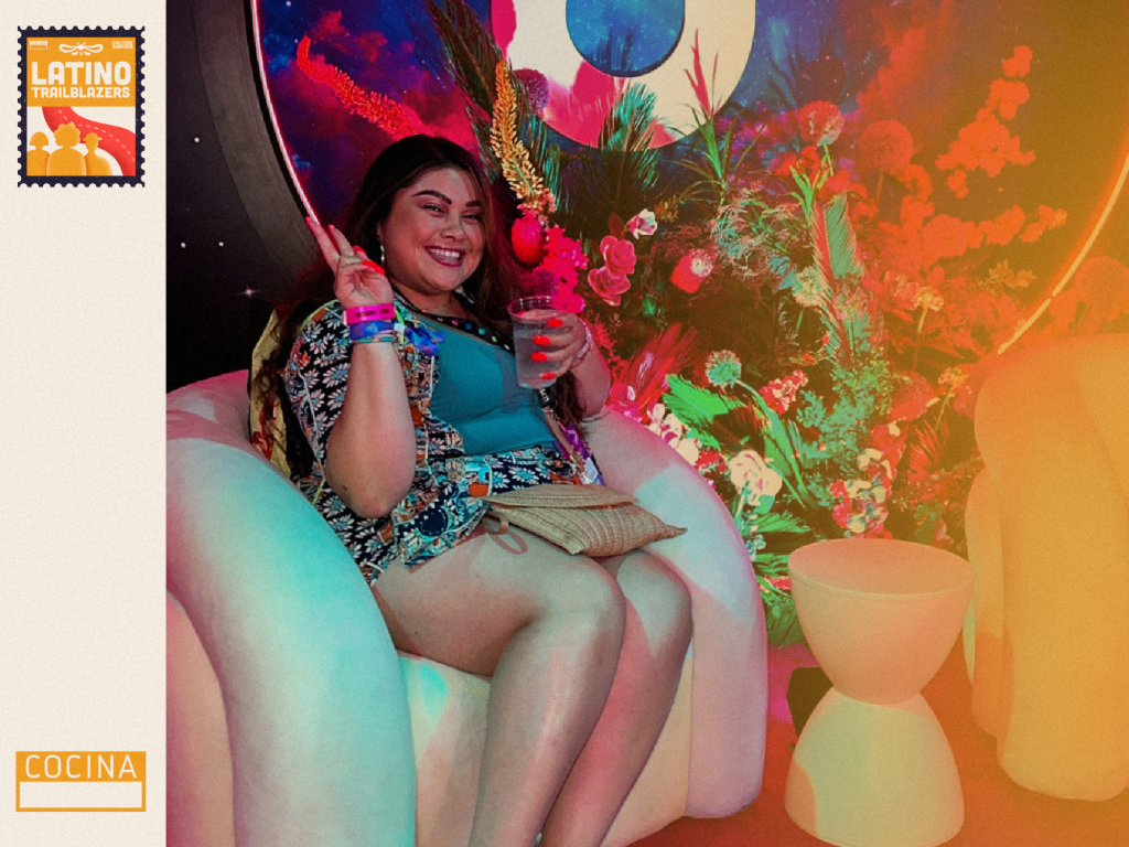 Jenny Solares, part of Latino Trailblazers, smiles to the camera and makes the peace sign with her fingers, while sitting in a couch at a party looking setting. Photo courtesy of Jenny Solares.
