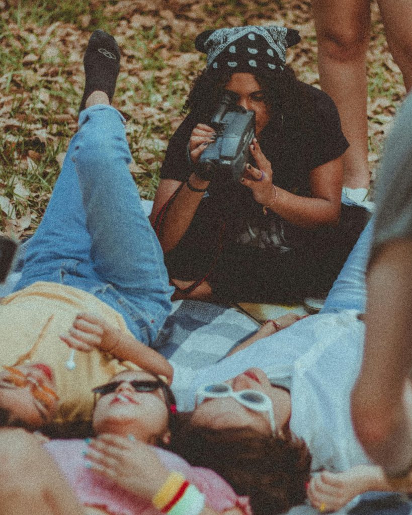 Camila Fernández's 6 Gift Picks for a Heartfelt Holiday - A person is filming the rest of their family and friends group while they enjoy a lazy day out, laying on top of a blanket in the midst of nature. Photo via Pexels, by Aline Viana Prado