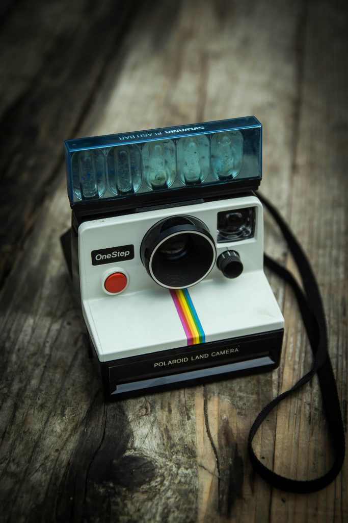Camila Fernández's 6 Gift Picks for a Heartfelt Holiday - White Polaroid camera on top of wood floor. Photo via Pexels, by Paul Seling